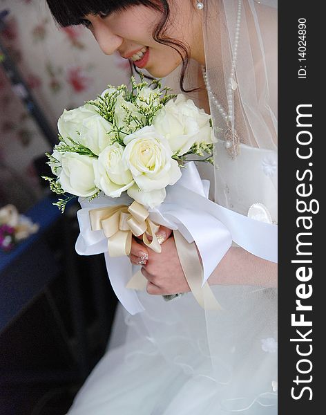 A beautiful chinese  bride looks down at her bouquet. She is dressed in a simple gown and wearing a tiara. A beautiful chinese  bride looks down at her bouquet. She is dressed in a simple gown and wearing a tiara.