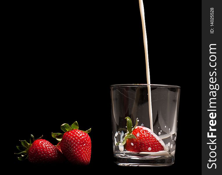 Strawberries in a glass on black background with pouring milk