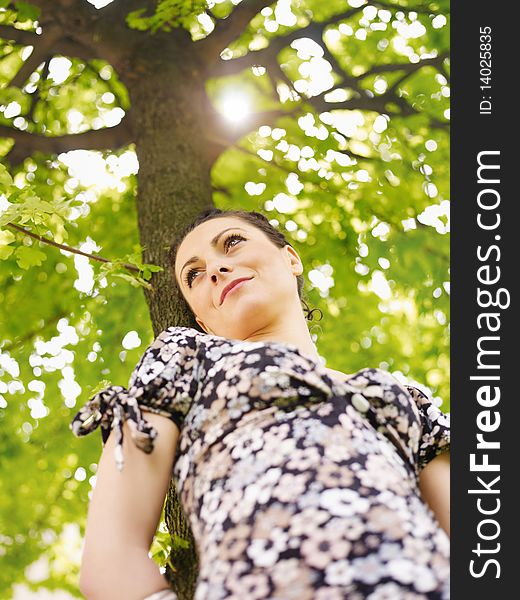 Potrait of attractive caucasian woman leaning on tree at sunset and looking away. Low angle view, vertical shape. Potrait of attractive caucasian woman leaning on tree at sunset and looking away. Low angle view, vertical shape