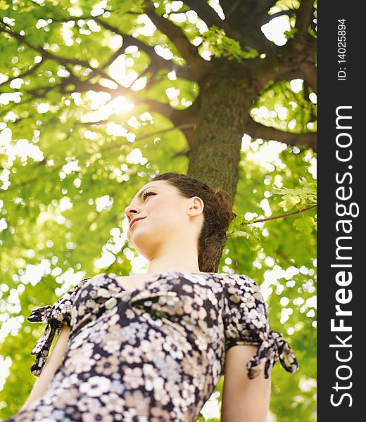 Potrait of sad woman leaning on tree at sunset and looking away. Low angle view, vertical shape. Potrait of sad woman leaning on tree at sunset and looking away. Low angle view, vertical shape