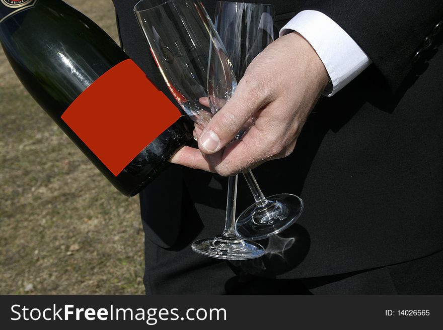 A man in suit holding two wine glasses and bottle of wine with a red label, good for copyspace. A man in suit holding two wine glasses and bottle of wine with a red label, good for copyspace