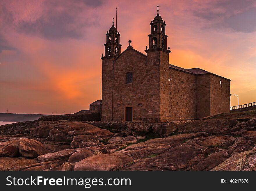 The Church of Virgen de la Barca, Muxia, Galicia, Spain shot at sunset, lots of orange and purples in the sky from a low angle