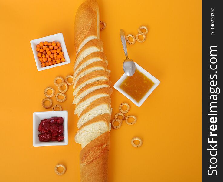 Top view of sliced french bread, jam, cottage cheese and butter on orange background. Appetizing still life of baking and jam. Top view of sliced french bread, jam, cottage cheese and butter on orange background. Appetizing still life of baking and jam