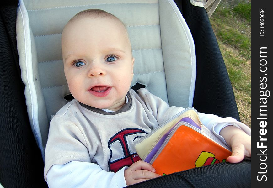 7 month old curious baby boy in pram with a book