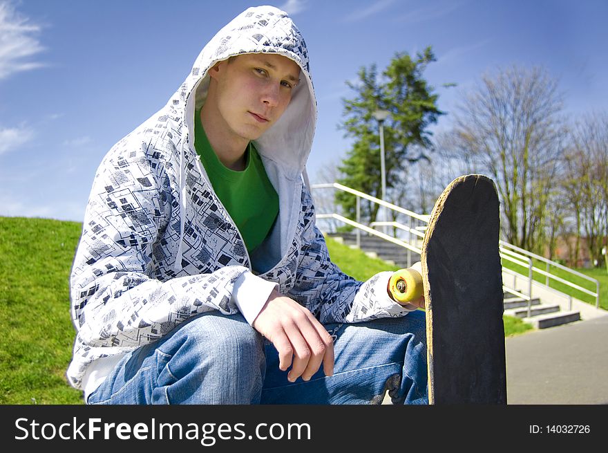 Teenage skateboarder conceptual image. Teenage skateboarder sits in skatepark.