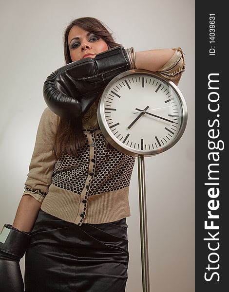 Young woman posing by the clock, wearing boxing gloves and looking self-confident. Young woman posing by the clock, wearing boxing gloves and looking self-confident