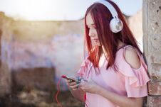 Redheads Teenager Girl Using Smartphone And Headphones, Listen To Music On Retro Ruins Wall Stock Photos