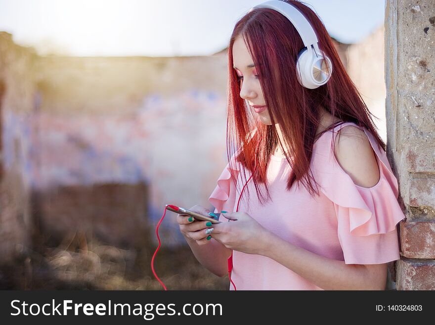 This captivating image portrays a young redhead teenager girl enjoying a moment of solitude and musical bliss against the backdrop of a mesmerizing sunset. Sitting alone on a retro ruins wall, she is fully immersed in her smartphone and wearing a headset, indulging in the pleasure of her favorite tunes. The close-up shot and selective focus draw attention to the teenager's expressive face, revealing her deep engagement with the music. Her eyes are closed, and a serene smile graces her lips, reflecting the joy and emotional connection she feels. The blurred background adds to the dreamlike ambiance, emphasizing the focus on her and the music she's listening to. The juxtaposition of the old ruins wall with the modern smartphone and headset symbolizes the blending of past and present, showcasing the universal and timeless nature of music's ability to transport us to another world. The warm tones of the sunset provide a soft, golden glow, creating a tranquil and magical atmosphere. This image captures the essence of solitude, self-expression, and the power of music to transport us. It resonates with teenagers and music enthusiasts who seek moments of introspection and escape. It is perfect for artistic projects, music-related promotions, social media campaigns, and any visual content that aims to evoke a sense of nostalgia, serenity, and the transformative power of music. This captivating image portrays a young redhead teenager girl enjoying a moment of solitude and musical bliss against the backdrop of a mesmerizing sunset. Sitting alone on a retro ruins wall, she is fully immersed in her smartphone and wearing a headset, indulging in the pleasure of her favorite tunes. The close-up shot and selective focus draw attention to the teenager's expressive face, revealing her deep engagement with the music. Her eyes are closed, and a serene smile graces her lips, reflecting the joy and emotional connection she feels. The blurred background adds to the dreamlike ambiance, emphasizing the focus on her and the music she's listening to. The juxtaposition of the old ruins wall with the modern smartphone and headset symbolizes the blending of past and present, showcasing the universal and timeless nature of music's ability to transport us to another world. The warm tones of the sunset provide a soft, golden glow, creating a tranquil and magical atmosphere. This image captures the essence of solitude, self-expression, and the power of music to transport us. It resonates with teenagers and music enthusiasts who seek moments of introspection and escape. It is perfect for artistic projects, music-related promotions, social media campaigns, and any visual content that aims to evoke a sense of nostalgia, serenity, and the transformative power of music.