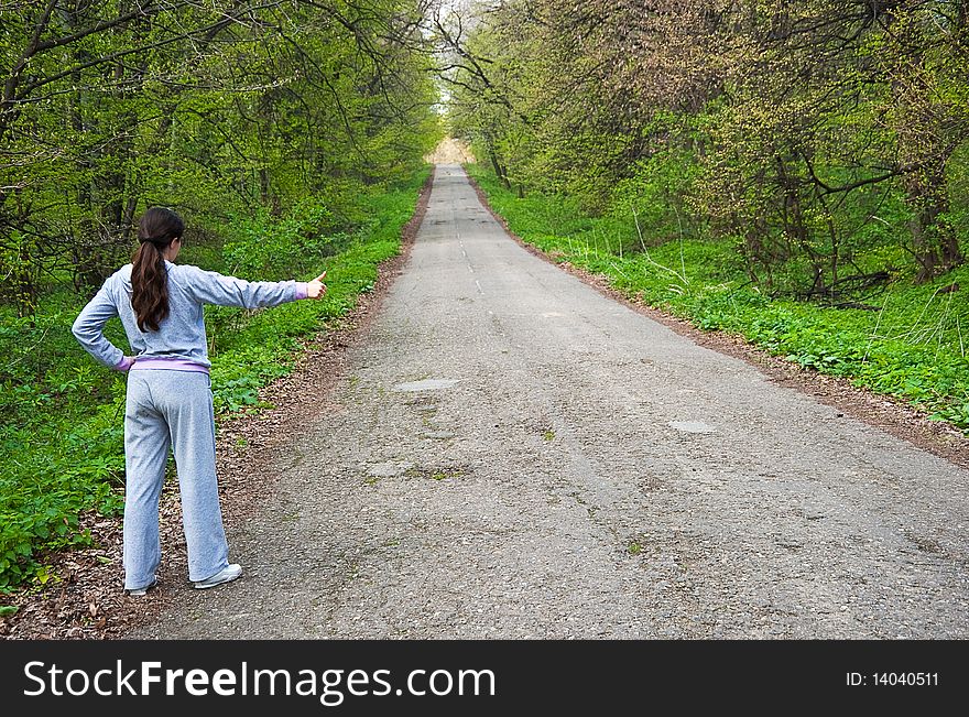 Girl hitch hiking near a road in the forest