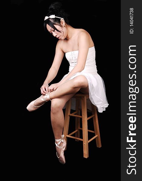 A Chinese ballet dancer in a white dress sitting on a chair and tying her
ballet slippers, for black background. A Chinese ballet dancer in a white dress sitting on a chair and tying her
ballet slippers, for black background.