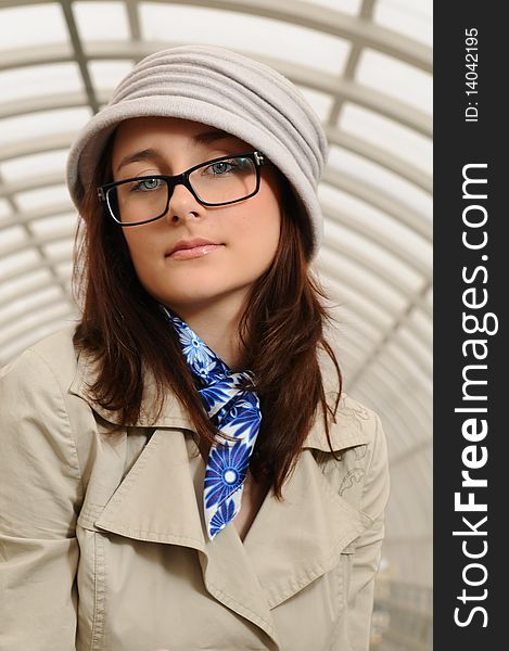 The young beautiful girl at station with a suitcase in a hand, in a light hat and a raincoat