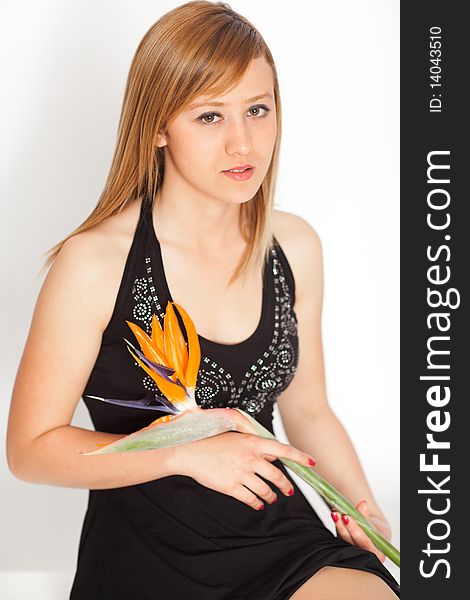 Young beautiful blonde woman with Bird of Paradise Flower ( Strelitzia reginae ) on white background smiling to camera, shallow depth of field, focus on eyes. Young beautiful blonde woman with Bird of Paradise Flower ( Strelitzia reginae ) on white background smiling to camera, shallow depth of field, focus on eyes