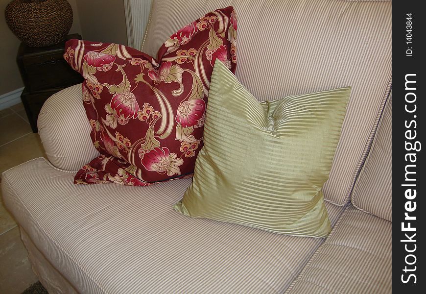 Two beautiful pillows on a couch or sofa one pillow is green stripes and one pillow is a print of flowers with red and pink colors. Two beautiful pillows on a couch or sofa one pillow is green stripes and one pillow is a print of flowers with red and pink colors