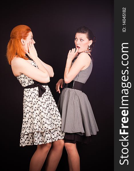 Two girls in dresses in retro style on a black background in studio