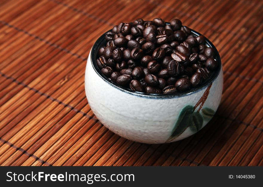 Coffee beans in a oriental-style cup, sitting on a  wooden place mat. Coffee beans in a oriental-style cup, sitting on a  wooden place mat.