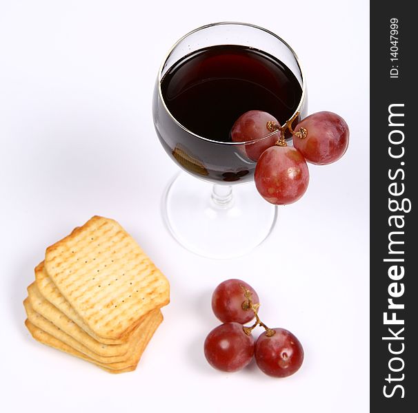 Red wine in a wineglass with red grapes and some crackers on white background