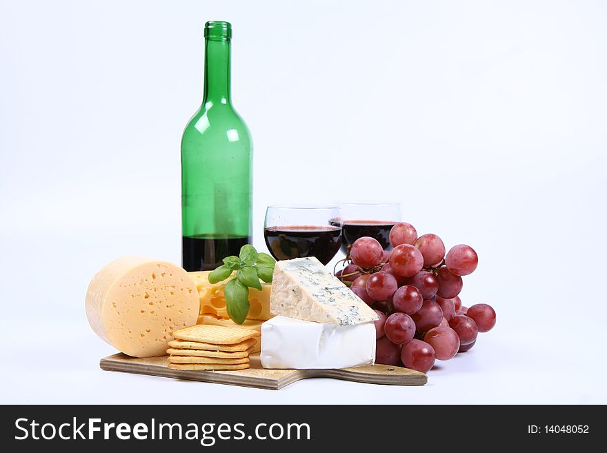 Various types of cheese (swiss, yellow, brie, blue cheese) with red wine, red grapes and crackers on white background