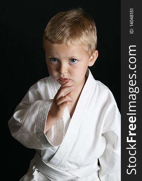 Young boy wearing his karate uniform on a black background. Young boy wearing his karate uniform on a black background