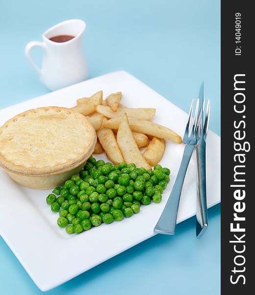An Australian meat pie served with peas and chips isolated against a blue background