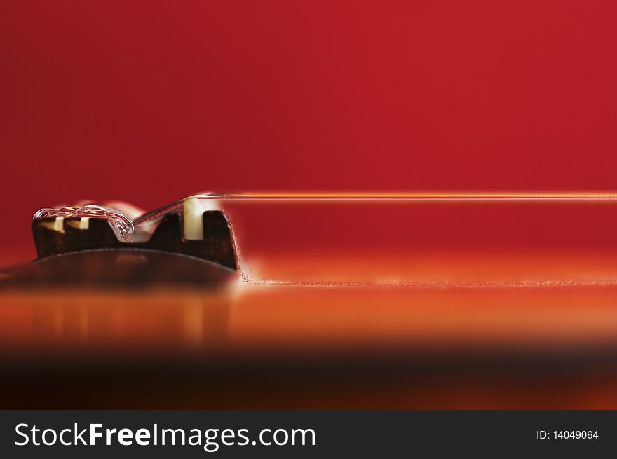 Guitar bridge and nylon strings on an out-of-focus red background. Guitar bridge and nylon strings on an out-of-focus red background.