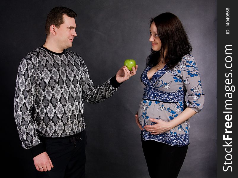 Careful man gives green apple pregnant woman on a black background. Careful man gives green apple pregnant woman on a black background
