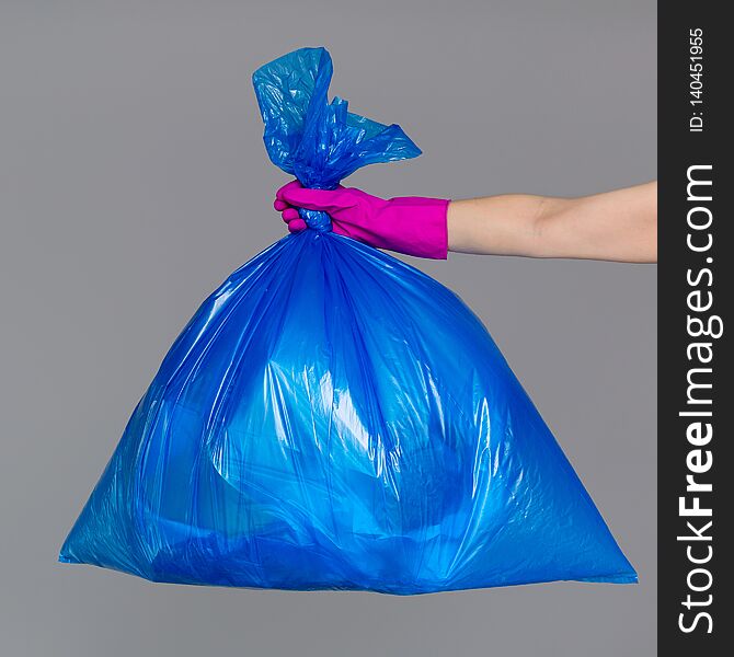 A woman`s hand in a rubber glove holds a blue plastic bag