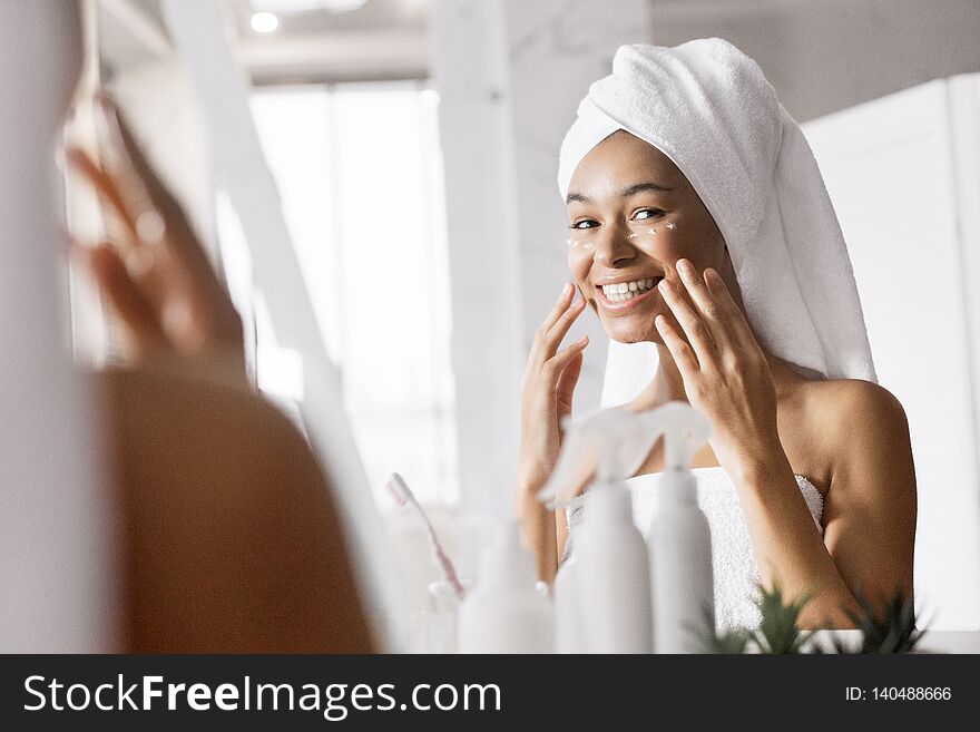 Smiling afro girl after shower with towel on head in bathroom looking in mirror. doing facial treatment. Smiling afro girl after shower with towel on head in bathroom looking in mirror. doing facial treatment.