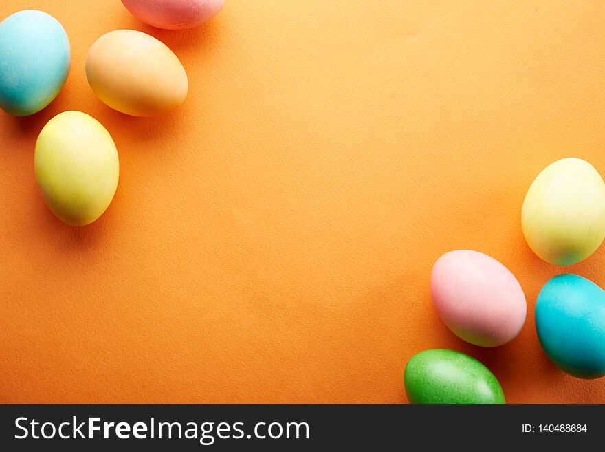 Bunch of blank painted Easter eggs of different pastel color on bright orange paper background with a lot of copy space for text. Top view, flat lay, close up. Easter greeting card concept. Bunch of blank painted Easter eggs of different pastel color on bright orange paper background with a lot of copy space for text. Top view, flat lay, close up. Easter greeting card concept