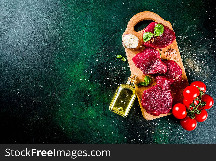 Raw beef meat steaks, with olive oil and spices, dark green concrete background copy space top view