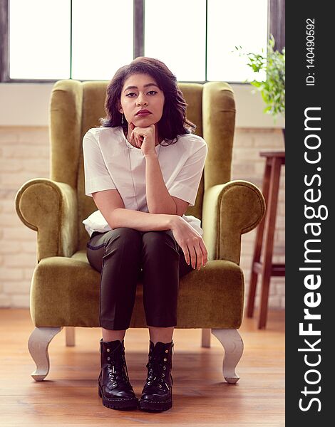 Serious look. Beautiful dark haired woman looking at you while sitting in the armchair