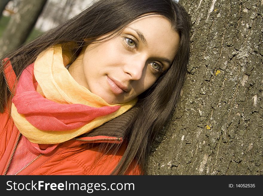 Beautiful female in a red jacket in the park based on the tree. He smiles and looks into the distance. Beautiful female in a red jacket in the park based on the tree. He smiles and looks into the distance