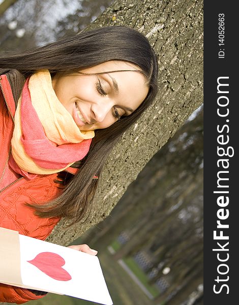 Beautiful female in the park. In the hands of an envelope with a letter. The letter pasted red heart. Beautiful female in the park. In the hands of an envelope with a letter. The letter pasted red heart