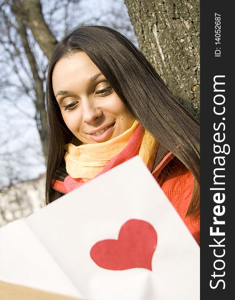 Beautiful female in the park. In the hands of an envelope with a letter. The letter pasted red heart. Beautiful female in the park. In the hands of an envelope with a letter. The letter pasted red heart
