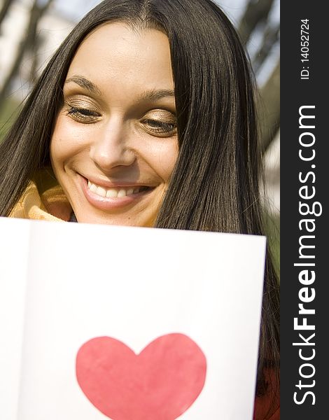 Beautiful female in the park. In the hands of an envelope with a letter. The letter pasted red heart. Beautiful female in the park. In the hands of an envelope with a letter. The letter pasted red heart