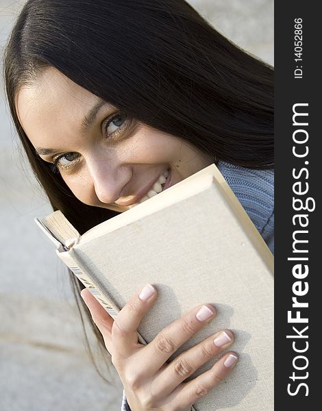 Beautiful female sitting on the stairs with a book. He smiles and looks into the frame. Beautiful female sitting on the stairs with a book. He smiles and looks into the frame