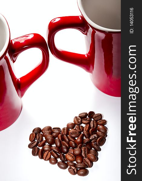 Coffee-beans heart against red cup`s handles on white backround