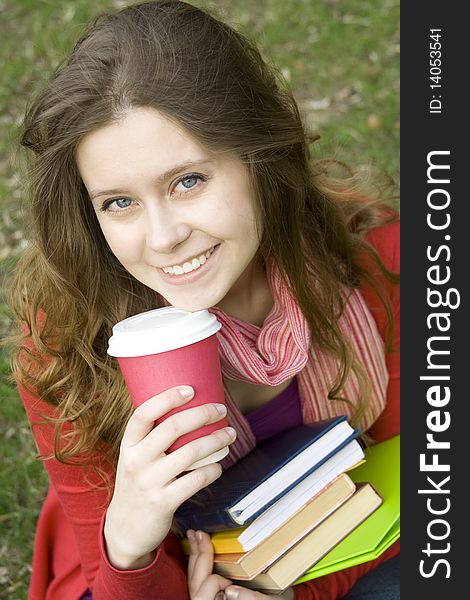 Young beautiful student at a dinner in the park sits on the green grass drinks coffee. Keep lots of books and folders. Young beautiful student at a dinner in the park sits on the green grass drinks coffee. Keep lots of books and folders