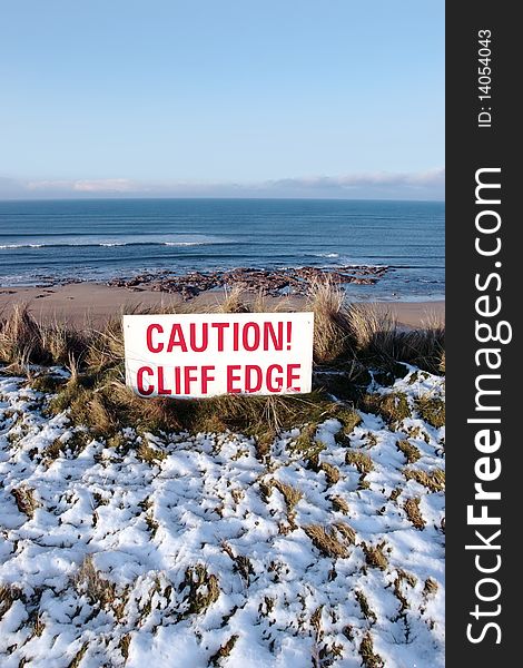 A red caution sign on a cliff edge in snow covered ballybunion