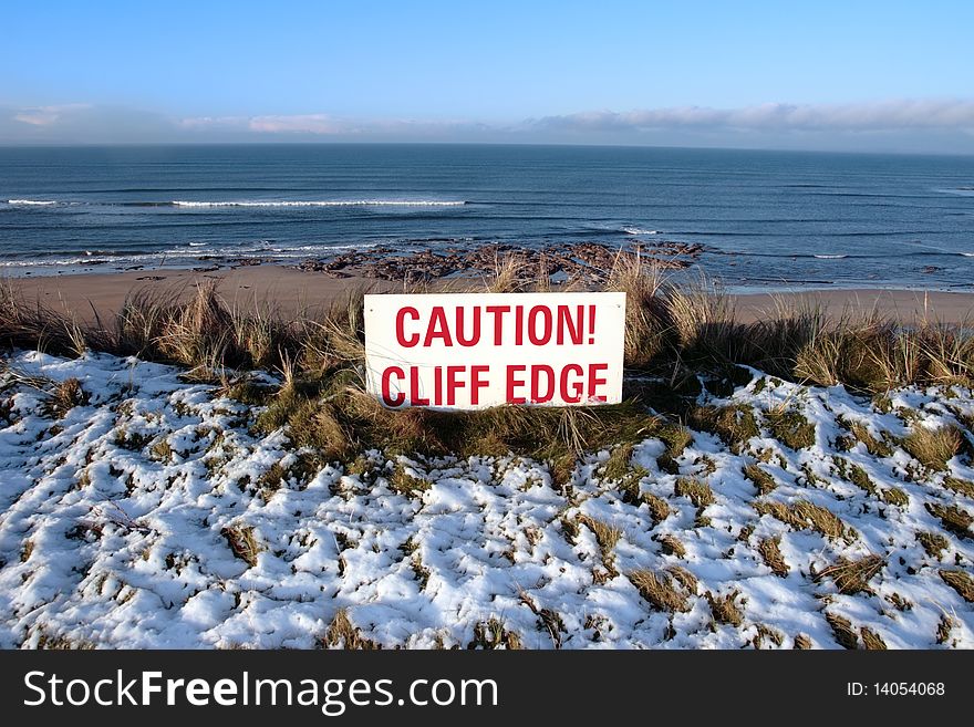 A red caution sign on a cliff edge in snow covered ballybunion. A red caution sign on a cliff edge in snow covered ballybunion