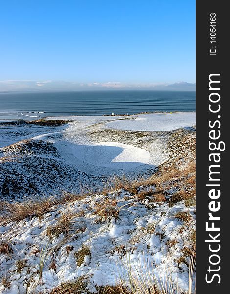 Snow covered links golf course in ireland in winter with sea background. Snow covered links golf course in ireland in winter with sea background