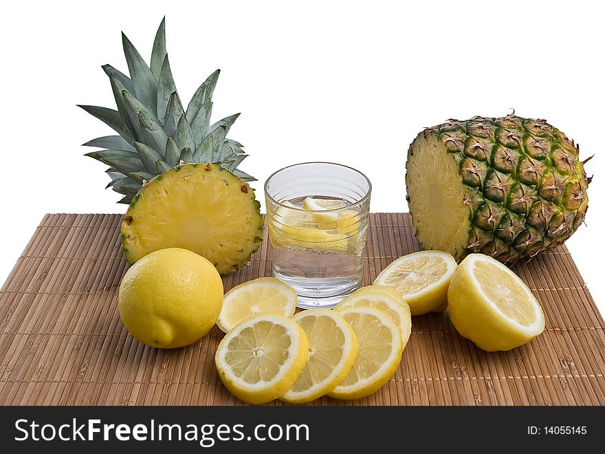 Pineapple with lemons and glass on bamboo mat isolated on white