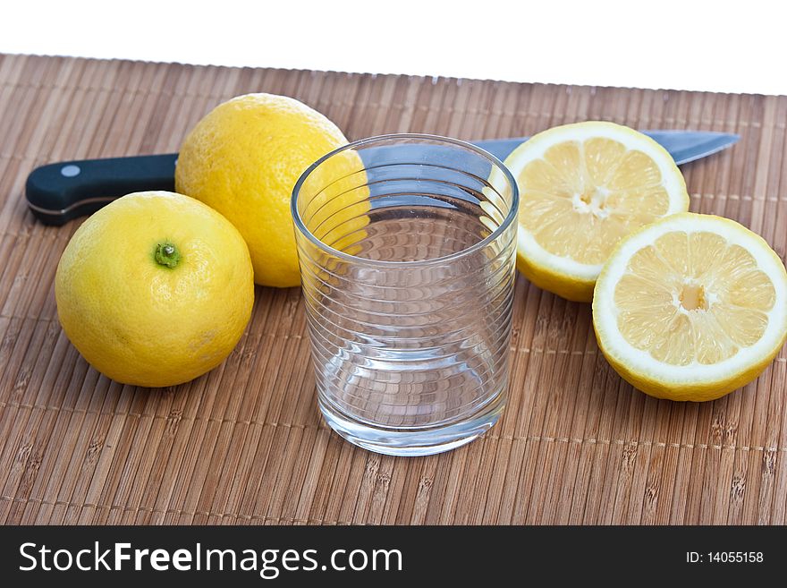 Lemon fruits with kitchen knife and glass on bamboo mat isolated on white. Lemon fruits with kitchen knife and glass on bamboo mat isolated on white
