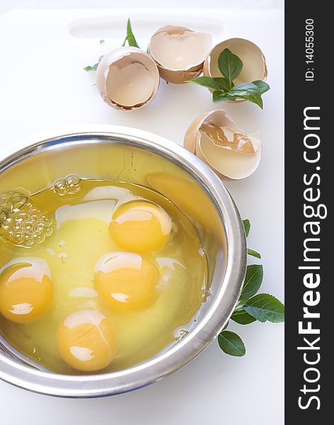 Eggs in the metal bowl with leafs on white cutting board
