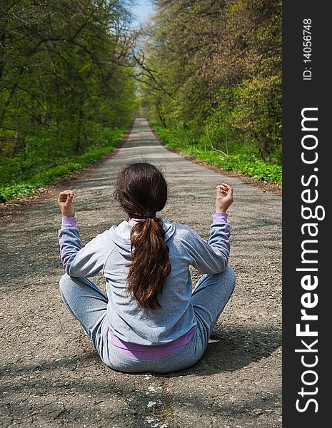 Young woman, sitting in the middle of the mountain road with her back facing a camera, waiting for something as she's meditating. Young woman, sitting in the middle of the mountain road with her back facing a camera, waiting for something as she's meditating