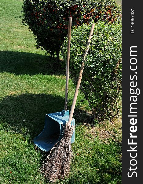 Broom and long handle scoop in the park near the bushes on the grass n the summer. Broom and long handle scoop in the park near the bushes on the grass n the summer.