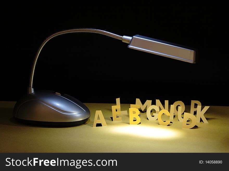 Luminous table lamp and letters cutting from yellow paper standing on dark background