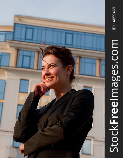 Young smiling businesswomen in black coat in fromt of glassy businesscenter