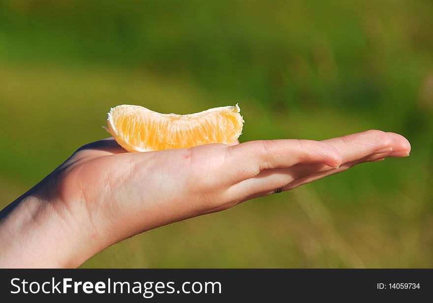 Segment of a juicy orange on a hand of the young girl