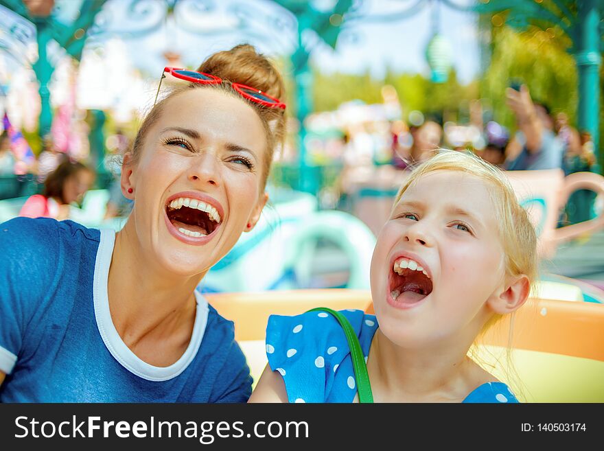 Smiling modern mother and child travellers in amusement park enjoying ride