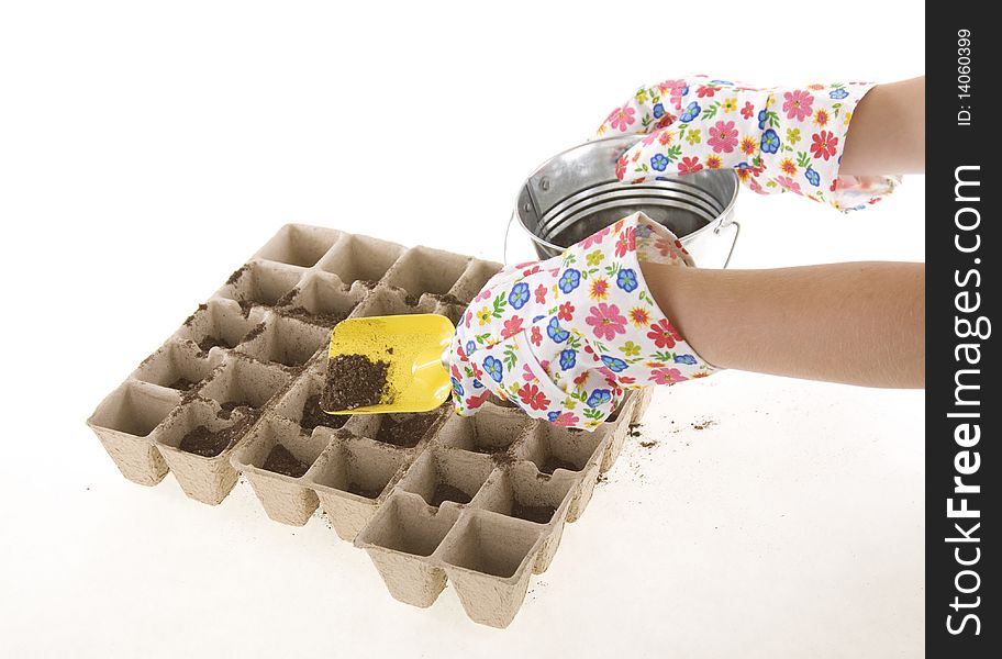 Gardener wearing colorful flower patterned  gardening gloves is using a yellow shovel to place soil from a silver pail into eco-friendly Composted Cow Manure Pots used for transplants- environmentally responsible seed starters. isolated on white 6200. Gardener wearing colorful flower patterned  gardening gloves is using a yellow shovel to place soil from a silver pail into eco-friendly Composted Cow Manure Pots used for transplants- environmentally responsible seed starters. isolated on white 6200